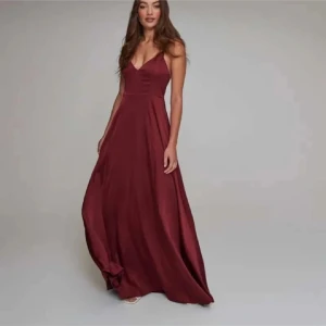 Vinröd långklänning med smala axelband - Säljer en super fin vinröd långklänning med smala korsade axelband och v-ringad urringning. Ger en snygg och modern look. Perfekt för bal eller fest. Sytt upp ett par cm men nuddar marken då jag ör 157♥️