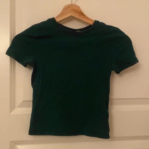 Mörkgrön t-shirt från Divided H&M - En basic mörkgrön t-shirt från Divided H&M i storlek XXS. Modellen är klassisk med rund halsringning och korta ärmar. Perfekt att matcha med jeans eller kjol för en enkel och clean look.