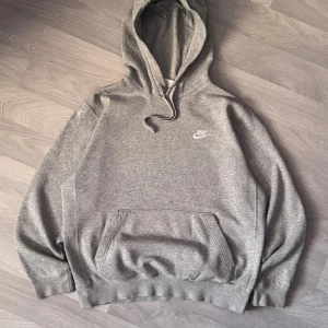 Grå Nike hoodie med broderad logo - Grå hoodie från Nike med broderad vit logga på bröstet. Ända defekten är lite missfärgad på vänsterärmen (visad på bild) som knappt är synlig.
