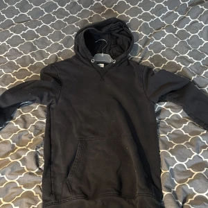 Svart hoodie från Pier One - Svart hoodie från Pier One med klassisk känguruficka och huva. Tröjan har långa ärmar och en enkel, stilren design utan tryck eller mönster. Perfekt för dig som gillar en basic look och vill ha något bekvämt att slänga på sig.