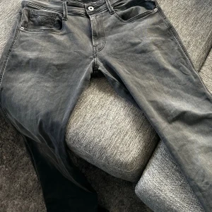 Replay Anbass grå jeans, storlek 31 - Snygga grå jeans från Replay, modell Anbass. Klassisk femficksdesign med Replay-logga på fickan och svart patch bak. Jeansen har en rak passform och är tillverkade i mjukt jeanstyg som sitter skönt hela dagen. Perfekt för dig som gillar stilrena och moderna jeans.