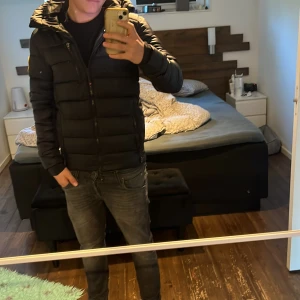 Svart pufferjacka från zavetti Canada - Säljer en svart pufferjacka från zavetti Canada med huva och dragkedja. Jackan har en patch på ärmen, diskreta fickor med dragkedja och en snygg logga på ryggen. Perfekt för kalla dagar och riktigt skön passform.