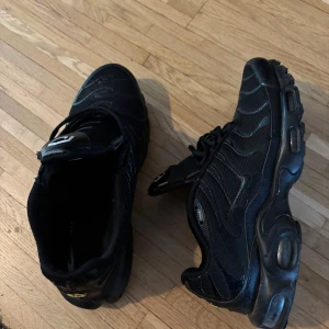 Svarta Nike Air Max sneakers - Säljer ett par svarta Nike Air Max sneakers med klassisk luftsula och mesh-överdel. Skorna har svarta snören, diskreta silverdetaljer och en sportig vibe. Perfekta för dig som gillar streetstyle och vill ha bekväma skor med snygg design.
