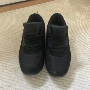 Nike Air Max 90 Triple Black sneakers - Säljer ett par helsvarta Nike Air Max 90 sneakers med klassisk siluett. Skorna har mesh och syntet på ovandelen, snörning och den ikoniska Air Max-dämpningen i sulan. Perfekta för dig som gillar en clean och stilren look. Jag har 42 men dom är lite små i storleken så tror en med storlek 39-40 kan ha dom
