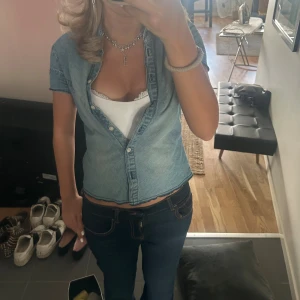 Ljusblå croppad jeansskjorta - Säljer en ljusblå croppad jeansskjorta med korta ärmar och knappar framtill. Skjortan har en avslappnad passform och är tillverkad i klassiskt jeanstyg. Perfekt för en cool och avslappnad stil.