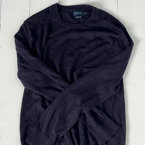 Svart merinoullströja från Riley - En svart, klassisk långärmad tröja från Riley i mjuk merinoull. Tröjan har rund halsringning och ribbade muddar vid ärmslut och nederkant. Perfekt för lager-på-lager och håller dig varm under kyliga dagar. Står storlek xl men den har blivit mindre i tvätten så den är ungefär s-m