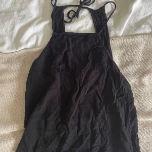 Svart topp ifrån hm  - Svart topp från Divided med tunna axelband och knytning i nacken. Toppen är ärmlös och har en enkel, stilren design i lätt och luftig bomull. Perfekt för varma dagar när du vill ha något bekvämt och snyggt.