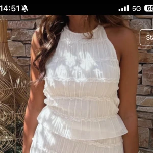 Vit topp  med snörning - Superfin vit topp i lätt och luftig bomull med volangdetaljer och ribbade partier. Toppen har hög hals, öppen rygg och smala snören som knyts baktill för en snygg passform. Perfekt för varma dagar och somriga vibes.