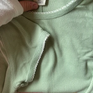 Ribbad ljusgrön t-shirt med spetskant - Superfin ljusgrön ribbad t-shirt med korta ärmar och vit spetskant vid halsringning och ärmslut. Första bilden är rätta färgen! 