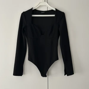 Svart långärmad bodysuit Gina Tricot XS - Svart långärmad bodysuit från Gina Tricot i storlek XS. Toppen har en markerad byst, fyrkantig urringning och figurnära passform. Tillverkad i stretchigt material som sitter snyggt på kroppen. Perfekt att styla med jeans eller kjol.