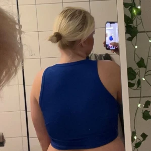 Blå croppad linnetopp - Snygg blå croppad linnetopp med hög halsringning och ärmlös design. Toppen har en tight passform och är tillverkad i ett stretchigt material som sitter skönt mot kroppen. Perfekt för dig som gillar sportig och trendig stil.