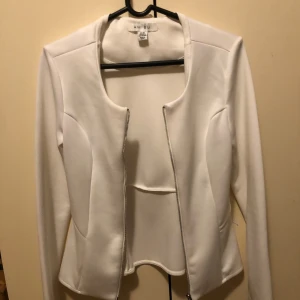 Vit kavajjacka från Amisu - Snygg vit kavajjacka från Amisu med lång ärm och dragkedja framtill. Jackan har en stilren, figurnära passform och är tillverkad i ett mjukt, slätt material som ger en clean look. Perfekt för dig som gillar minimalistisk stil.