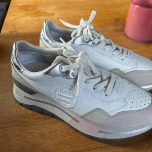 Vita sneakers från bagatt i äkta skin - Snygga vita sneakers från Bagatt med silvriga detaljer och logga på sidan. Skorna har snörning, perforerad tå och en sula i grått och rosa. Tillverkade i skinn och mocka för en fräsch och modern look. Endast andvända 2 gånger.