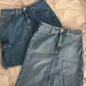 Två jeanskjolar i olika blå nyanser - Säljer två snygga jeanskjolar, en i mörkblå denim med rå kant och en i ljusblå denim med klassisk fåll. Båda har fickor fram och bak, bälteshällor och dragkedja med knapp. Perfekta för dig som gillar enkel och cool stil.