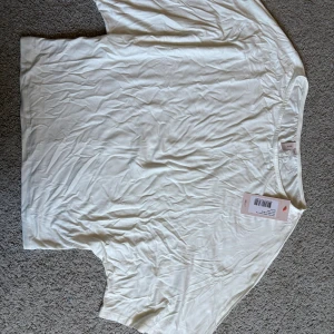 Vit enkel topp från Nelly XS - Säljer en vit, stilren topp från Nelly i storlek XS. Toppen har rund hals och är kortärmad, perfekt för dig som gillar minimalistisk stil. Materialet är mjukt och lätt bomull, vilket gör den skön att bära. En klassisk basic som funkar till allt.