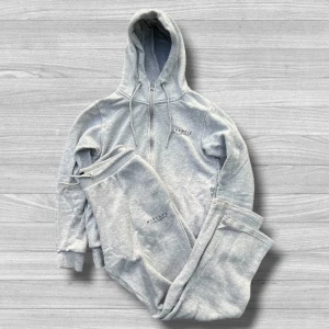  McKenzie tracksuit - Ljusgrå tracksuit från McKenzie med dragkedja, huva och snörning. Tröjan har ribbade muddar och liten logga på bröstet. Perfekt för chill dagar eller träning. Tillverkad i mjuk bomullsmix för extra komfort.