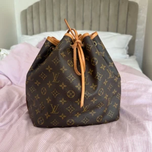 Louis Vuitton Monogram Noé axelväska - Säljer en klassisk Louis Vuitton Noé axelväska i brunt monogrammönster med ljusbruna skinnremmar och detaljer. Väskan har dragskostängning och ikoniska LV-loggor över hela ytan. Perfekt storlek för att bära allt du behöver och ger en lyxig touch till din outfit. Perfekt skick. Fler bilder skickas privat!! Lite smutsig på undersidan. Har genomgått äkthetskontroll då den är köpt från Vestiaire, se sista bilden🥰