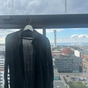 Svart linneskjorta från Riley, M - Svart skjorta från Riley i luftig och tunn linnematerial. Klassisk krage och långärmad modell, perfekt för dig som gillar stilrena och enkla plagg. Skjortan har en snygg, rak passform och känns riktigt chill att bära under varmare dagar. Ordinarie pris är 899kr