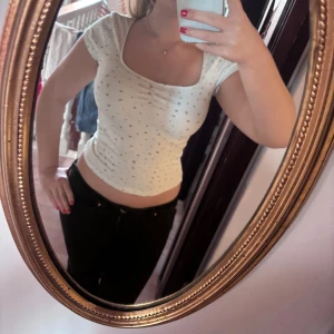 Vit croppad topp med små blommor - Säljer en vit croppad topp med små blommor som mönster. Toppen har korta ärmar, rundad halsringning och sitter tight mot kroppen. Perfekt för dig som gillar gulliga detaljer och en feminin stil. Materialet känns mjukt och stretchigt, bomull med lite syntet.