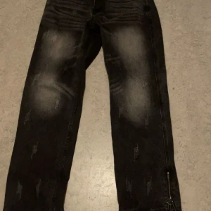 Svarta jeans med dragkedja och slitningar - Svarta jeans med coola slitningar och blekta detaljer på både fram- och baksida. De har en dragkedja vid benslutet som ger en edgy vibe. Jeansen har klassisk femficksdesign och är tillverkade i jeansmaterial.