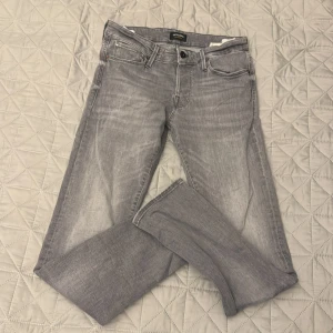 Grå jeans från Jack & Jones, 29/30 - Snygga grå jeans från Jack & Jones i modellen Slim Glenn. Jeansen har klassisk femficksdesign, normal midja och raka ben. Materialet är mjukt denim i bomull med en lätt tvättad look. Perfekta för dig som gillar en stilren och enkel vibe.