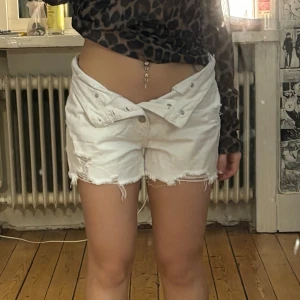 Vita jeansshorts med knappar - Säljer ett par vita jeansshorts med hög midja och flera silverfärgade knappar framtill. köpta på outlet i usa, passar 34-38