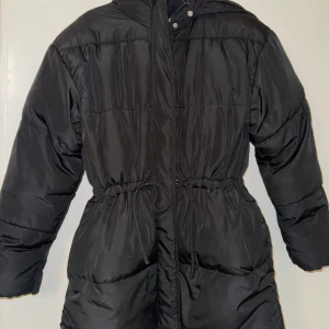 Svart pufferjacka med huva - Säljer en svart pufferjacka med huva och snörning i midjan. Från HM