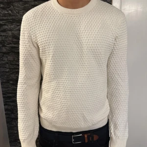 Vit stickad tröja från East West - Säljer en vit stickad tröja från East West med snyggt strukturerat mönster. Tröjan har rund halsringning, ribbade muddar och lång ärm. Köpt på Åhléns, nypris 800kr 