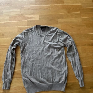 Beige rundhalsad tröja Oscar Jacobson - Säljer en stilren beige rundhalsad tröja från Oscar Jacobson i mjuk bomull. Tröjan har ribbade muddar vid hals, ärmslut och nederkant. Perfekt för lager-på-lager och funkar året runt. Klassisk och enkel design som passar till allt.