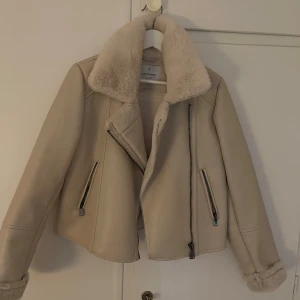 Beige teddyjacka från Stradivarius - Säljer en beige teddyjacka från Stradivarius med fluffig krage och foder. Jackan har två snedställda dragkedjefickor och en snygg asymmetrisk dragkedja framtill. Perfekt för dig som gillar en chill och trendig look med lite extra cozy-vibe. Priset kan diskuteras 