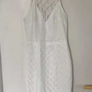 Vit studentklänning  spetsklänning med meshdetaljer - Säljer en vit kortklänning med snygga spets- och meshdetaljer. Klänningen har ärmlös design, v-ringad hals och dragkedja bak. Mönstret är rutigt med inslag av broderade detaljer som ger en cool och fräsch look. Perfekt för dig som gillar stilrena och trendiga plagg.