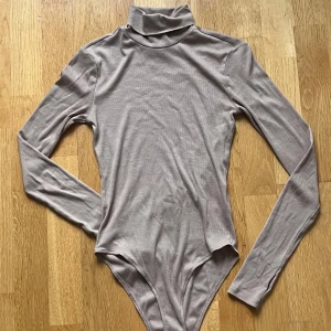 Beige polotopp-body från H&M XS - Säljer en beige polotopp-body från H&M i storlek XS. Toppen har lång ärm, hög krage och är tillverkad i ribbad, mjuk bomullsmix. Snygg slim passform som sitter tight mot kroppen och passar perfekt till jeans eller kjol. Ett litet hål på armen finns, 2mm.