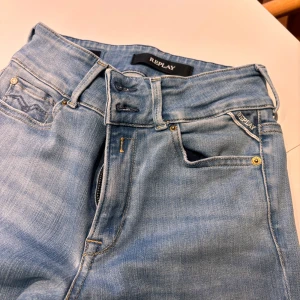 Ljusblå Replay jeans slim fit - Säljer ett par ljusblå jeans från Replay med klassisk femficksdesign och snygga detaljer på bakfickorna. Jeansen har slim passform och är tillverkade i mjukt denimtyg med dragkedja och knapp framtill. Perfekta för en avslappnad och trendig look.