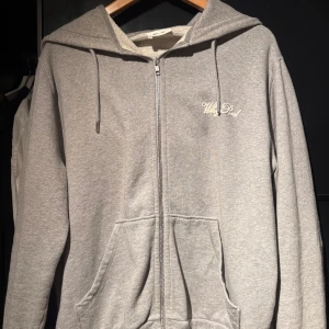 Grå hoodie från Whyred med dragkedja - Säljer en stilren grå hoodie från Whyred med broderad logga på bröstet. Tröjan har huva med snörning, två fickor framtill och hel dragkedja. Perfekt för chill dagar och enkel att matcha med jeans eller joggers.