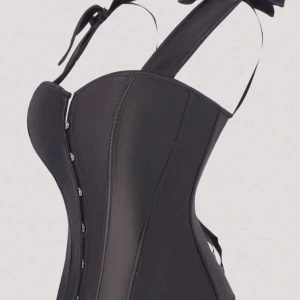 Svart korsett med snörning och breda axelband - Säljer en svart korsett med breda axelband som knyts med rosett. Framsidan har metallknappar och baksidan har snygg snörning med satinband. Korsetten har en figurnära passform och är tillverkad i ett syntetmaterial med lätt glansig finish.