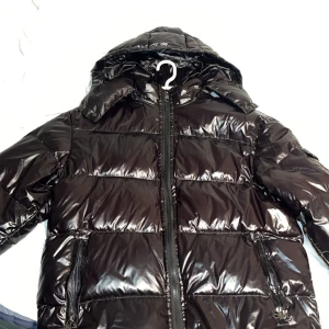 Moncler maya med huva - Säljer en svart pufferjacka från Moncler med glansig finish och huva. Jackan har dragkedja framtill, två sidofickor med dragkedja och Moncler-logga på ärmen. Perfekt för kalla dagar och har en riktigt snygg streetstil. Storlek M. Möts i Stockholm fraktas även