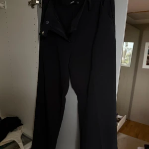 Svarta vida kostymbyxor från BikBok - Svarta kostymbyxor från BikBok i storlek 38. Byxorna har en klassisk rak och vid passform med dragkedja och knapp framtill. Perfekta för en clean och stilren look. 