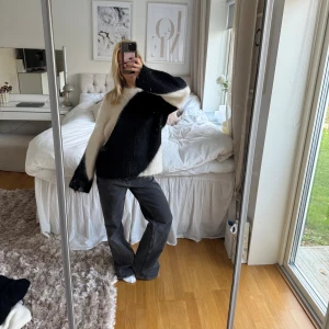 Stickad tröja - Säljer en riktigt snygg stickad tröja i svart och vitt med breda, långa ärmar. Tröjan har ett coolt, asymmetriskt mönster som ger en unik vibe. Materialet är mjukt och fluffigt, perfekt för att hålla sig varm under kyliga dagar. Passar dig som gillar statement-plagg.