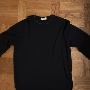 Mörkblå stickad tröja Gran Sasso - Mörkblå stickad tröja från Gran Sasso, tillverkad i Italien. Rund halsringning och långärmad modell med snygga grå mockadetaljer på armbågarna. Perfekt för dig som gillar stilrena och klassiska plagg med en twist. Tröjan är i väldigt bra skick och ingen användning syns. Storleken är 48 vilket motsvarar M. Tveka inte på att höra av er vid frågor!