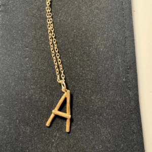 Guldhalsband med bokstav A Maria Nilsdotter - .Guldpläterat halsband från Maria Nilsdotter. Kedjan är 45cm lång. Materialet under pläderingen är silver. Pläderingen är något nött. Kommer med ask.