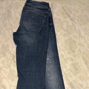 G-Star  jeans med slitningar - Snygga mörkblå jeans med diskreta slitningar framtill och klassiska bakfickor. Jeansen har en rak passform och är tillverkade i mjukt denimtyg. Fraktar samma dag vill få sålda snabbt. Storlek 31 passar lite mindre.