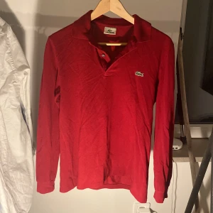 Vinröd långärmad pikétröja Lacoste - Säljer en vinröd långärmad pikétröja från Lacoste med klassisk krage och knappar framtill. Tröjan har det ikoniska krokodilmärket broderat på bröstet och är gjord i mjuk bomull. Perfekt för dig som gillar stilrena och sportiga plagg. Finns ingen storleksguide men passar S | 199 kr
