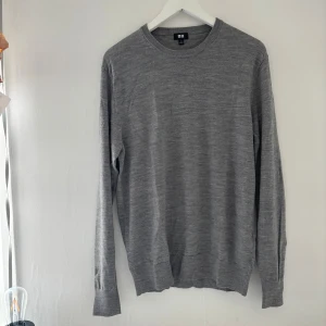 Grå merinoulltröja från Uniqlo - Snygg grå tröja från Uniqlo i mjuk merinoull. Klassisk rund hals och långärmad modell med diskret ribbade muddar. Perfekt för dig som gillar stilrena och enkla plagg med skön passform.