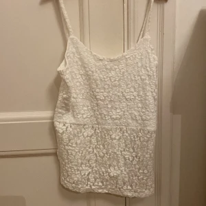 Vit spetslinne från Kappahl - Supersött vitt linne från Kappahl i storlek 158/164. Toppen har tunna axelband och är helt täckt av blommig spets som ger en romantisk vibe. Perfekt för varma dagar och att styla med jeans eller kjol. Spetsen är mjuk och har ett fint blommönster. Aldrig använd och har prislappen kvar