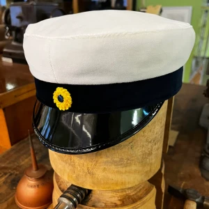 Studentmössa från CTH I lunda modellen st 52-63 - Klassisk studentmössa från CTH med vit ovandel i bomull, mörkblå sammetsband och blank svart skärm. Insidan är fodrad med rött tyg och har en gul blomliknande dekoration med blå mitt framtill. Perfekt för studenten och ger en riktigt traditionell look. Mössan är i Lunda modellen. Vid eventuella frågor va inte rädda att skriva till oss!