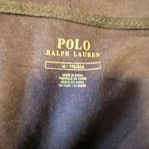 Marinblå hoodie från Polo Ralph Lauren - Snygg marinblå hoodie från Polo Ralph Lauren med dragkedja i guld, broderad logga på bröstet och huva med snörning. Tröjan har känguruficka och är tillverkad i mjuk bomull, perfekt för chill dagar eller när du vill ha en clean look.