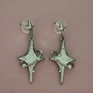 Silvriga stjärnörhängen med pärldetaljer -  örhängen i silverfärgad metall med cool stjärnform och små gnistrande stenar. Dekorerade med vita pärlor som ger en extra touch. 