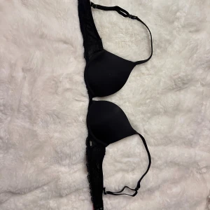 Svart push-up bh från Hunkemöller - Säljer en svart push-up bh från Hunkemöller i storlek 75AA. Bh:n har släta kupor och spetsdetaljer längs sidorna samt justerbara axelband för perfekt passform. Enkel och stilren design som funkar till allt.
