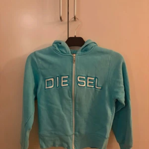 Turkos hoodie från Diesel med dragkedja - Snygg turkos hoodie från Diesel med broderad logga framtill. Tröjan har huva, långa ärmar och hel dragkedja. Perfekt för en chill och sportig look. Mjuk och skön, tillverkad i bomullsmix.