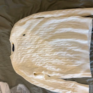 Vit kabelstickad tröja från Polo Ralph Lauren - Säljer en vit kabelstickad tröja från Polo Ralph Lauren med klassisk rund hals och långärmad design. Tröjan har det ikoniska lilla Polo-logot på bröstet och är tillverkad i mjuk bomull. Perfekt för dig som gillar stilrena och tidlösa plagg. L passar storlek m